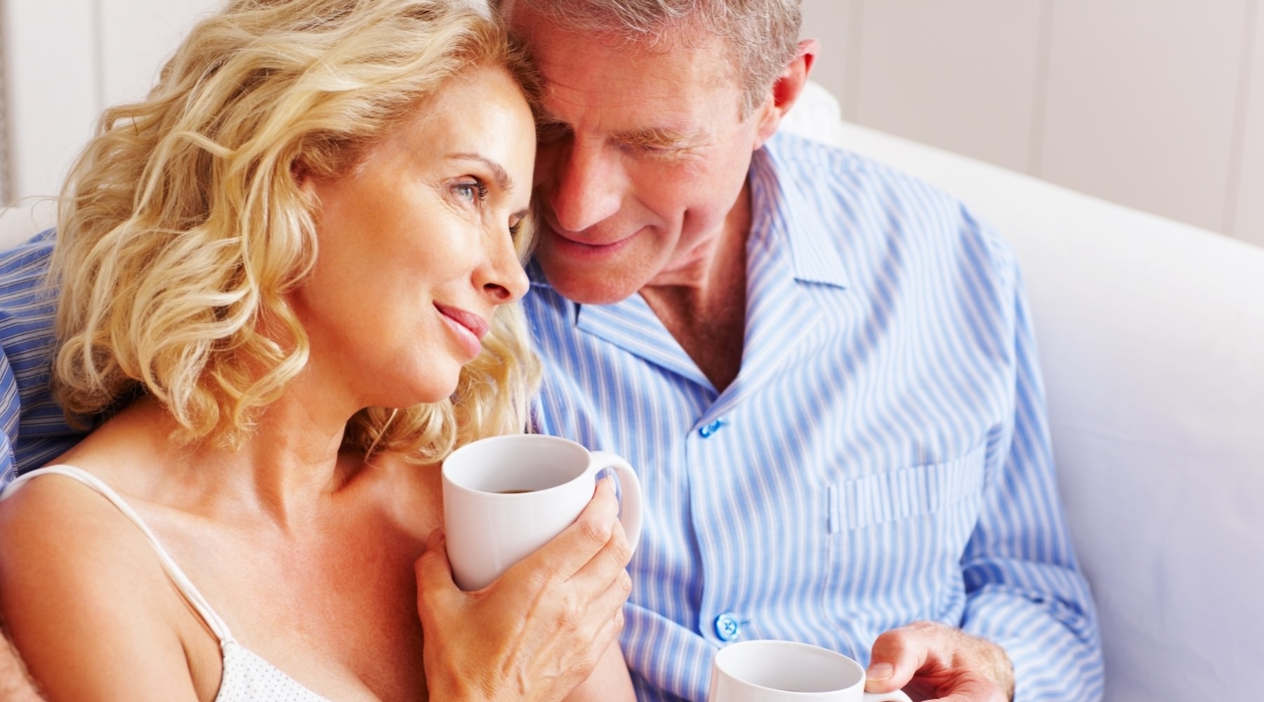 a man and a woman sitting on a couch holding coffee mugs
